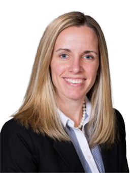 A woman, Amy Doll, with long blond hair in a dress coat and collared blue shirt smiles at the camera. 