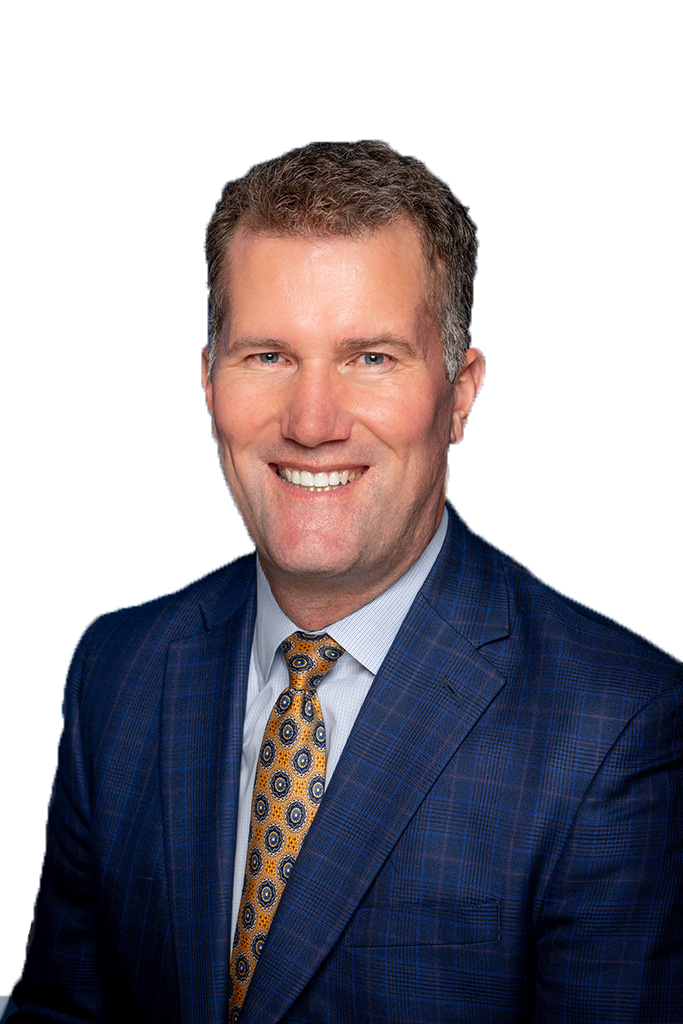 A man in a dark navy linen jacket with a yellow a blue polka dotted tie smiles at the camera. 