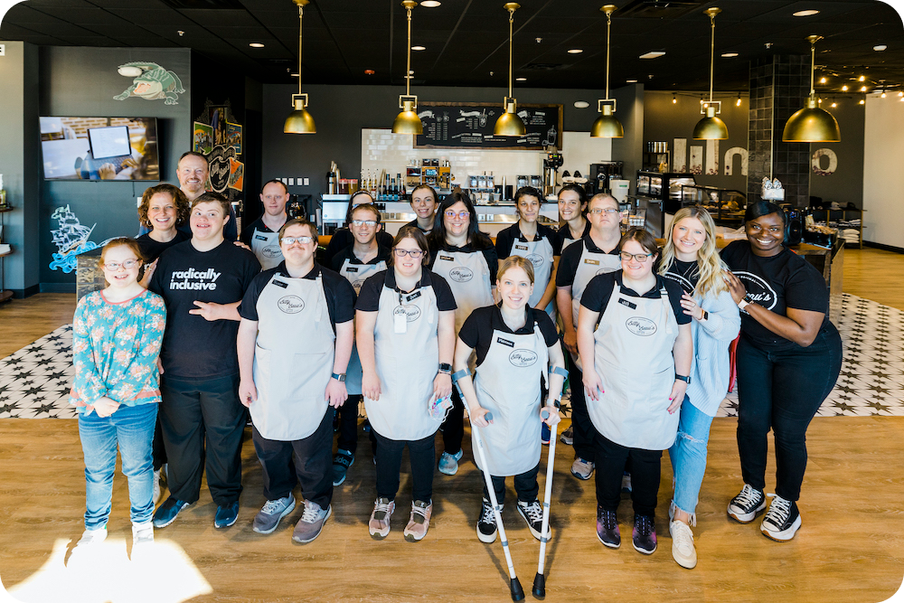 A group of Bitty a d Beau's employees posing in front of a cafe and smile at the camera.