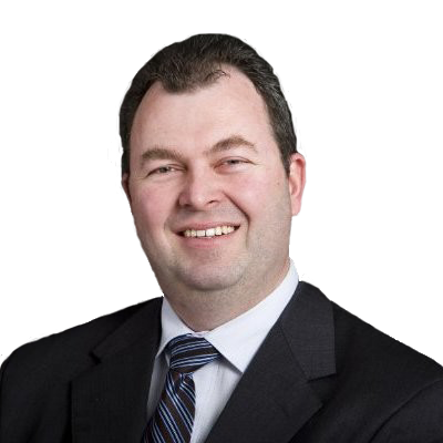 A man with short, dark hair in a black suit jacket and tie smiles at the camera. 